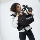 Person holding a camera with a SAKK backpack against a white background
