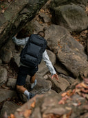 Person climbing rocky terrain wearing a black backpack