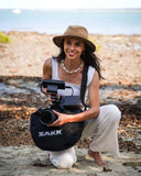Woman holding a camera with a SAKK bag on a beach